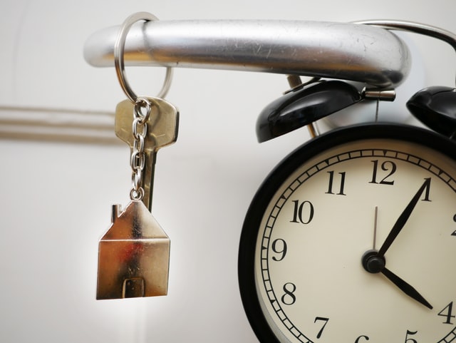 keys in door and door knob with clock hanging over it